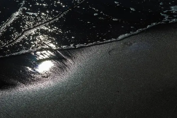 Büyüleyici bir siyah beyaz fotoğraf güçlü bir dalganın sahile çarptığı anı yakalıyor. Karanlık dalga ve aydınlık kum arasındaki zıtlık dramatik bir sahne yaratır.