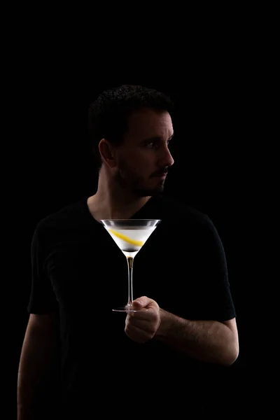 Siyah gömlekli genç adam siyah bir arka planda izole edilmiş bir bardak martini ile