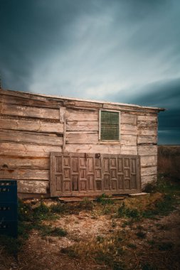 Penceresi ve kapısı olan küçük, eski bir bina. Kapı açık ve pencere de kapalı. Bina çimen ve toprakla çevrili.