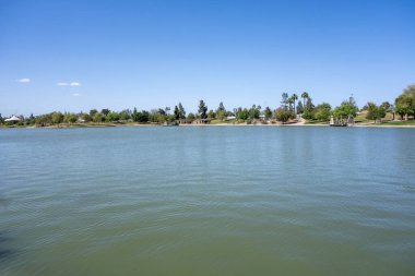 Kiwanis Park Gölü 'nün serin ve ferahlatıcı yeşil-mavi suları birkaç beyaz bulutla berrak gökyüzü altında, Tempe, Arizona 