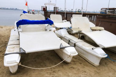 Elektrikli eğlence katamaranları sabahın erken saatlerinde San Diego, Kaliforniya 'da, Sail Bay' in üzerindeki kasvetli gökyüzünün altında, rıhtımın yanındaki kumsalda dinleniyorlar.