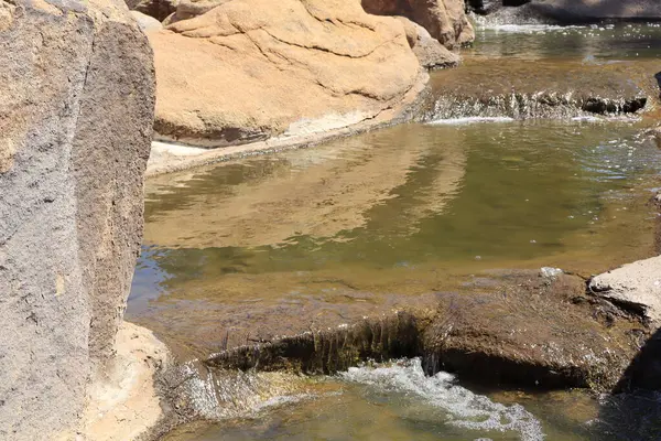 Büyük kayalar arasında yavaşça akan yeşilimsi sulardan oluşan küçük şelaleler.