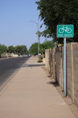 Bisiklet yolu tabelası kaldırıma kurulmuş. Sokak boyunca çitin yanında, Phoenix, Arizona 'da.
