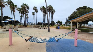 San Diego, CA - 12 Haziran 2024: Bonita Cove rıhtım parkında ilk sabah misafirlerini bekleyen açık hava hamağı hala boş Maruta Gardner oyun parkı 