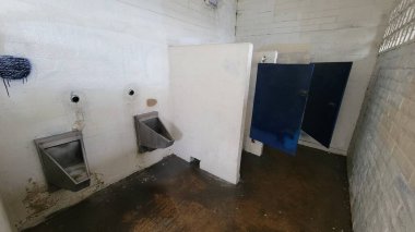 Islak zeminli umumi tuvalet paslanmaz çelik pisuvar, bakımsız duvarlar ve kilitleri kırık kapılar, Güney Pasifik Sahili, San Diego, California