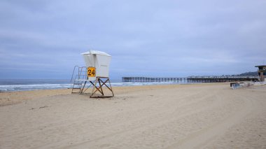 San Diego, Kaliforniya 'daki umumi ahşap iskelenin yakınındaki Pasifik sahilinin boş kumlarında cankurtaran kulübesi.