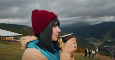 Dağlarda genç bir kadın gezgin sıcak bir içecekle ısınıyor. Sonbahar maceraları. Z kuşağı yolculuğu.