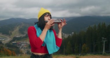 Dağlarda genç bir kadın gezgin sıcak bir içecekle ısınıyor. Sonbahar maceraları. Z kuşağı yolculuğu.