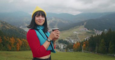 Dağlarda genç bir kadın gezgin sıcak bir içecekle ısınıyor. Sonbahar maceraları. Z kuşağı yolculuğu.