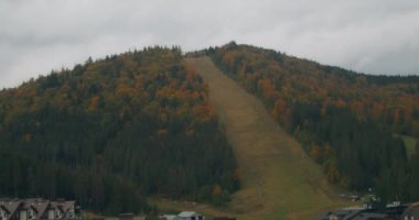 Bukovel kayak merkezinin manzarası, güzel sonbahar ağaçları ve dağlar, uzaktaki evler.