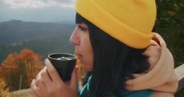 Dağlarda genç bir kadın gezgin sıcak bir içecekle ısınıyor. Sonbahar maceraları. Z kuşağı yolculuğu.