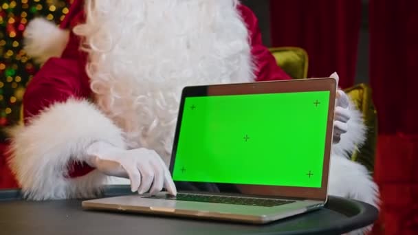 现代圣诞老人 快乐的圣诞老人坐在椅子上 背对着圣诞树 正在笔记本电脑上工作 面带微笑 — 图库视频影像