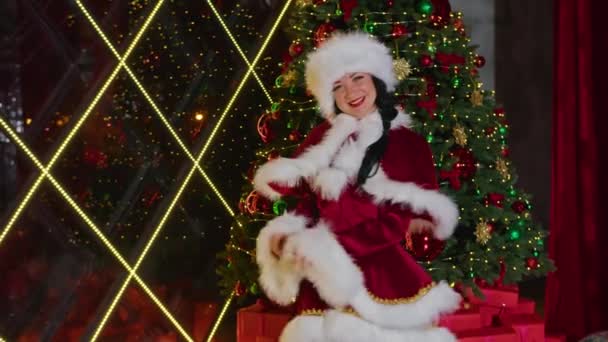 幸せな女性サンタさんは彼女のクリスマスオフィスでカメラのために笑顔 遊び心のある気分 隔離された休日だ 遠隔コミュニケーション休日の贈り物や割引 — ストック動画