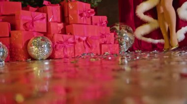 Altın ayakkabılı bir kadının bacakları ve Noel ağacının arkasında bir Noel elbisesi.