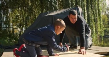 Mutlu baba ve oğul ağaçta bir ev inşa eder, bir çizime bakar, bir ağacı testereyle keser, tornavidayla kendi kendini becerir..