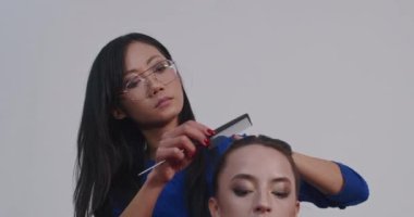 Profesyonel bir fotoğraf stüdyosunda kamera çekimi için modeller hazırlarken. Asyalı bir stilist ve Avrupalı bir makyöz modelleri boyayıp saçlarını yapıyorlar..