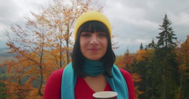 Dağlarda genç bir kadın gezgin sıcak bir içecekle ısınıyor. Sonbahar maceraları. Z kuşağı yolculuğu.