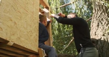 Mutlu baba ve oğul ağaçta bir ev inşa eder, bir çizime bakar, bir ağacı testereyle keser, tornavidayla kendi kendini becerir..