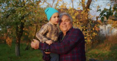 3 yaşındaki bir çocuk bahçede büyükbabasıyla elma toplamaktan mutlu olur, eğlenir, onları bir ağaçtan toplar, bir kovada toplar ya da dedesine verir..