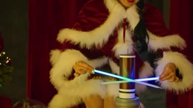 Noel Baba kostümlü mutlu kadın, Tesla bobininin yanındaki neon tüplerle Noel ağacının arka planında oynuyor. Yılbaşı şovu, çocuklar için tatil.
