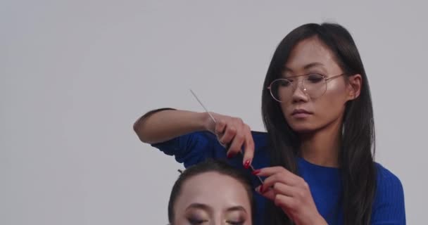 プロの写真スタジオでカメラ撮影のモデルを準備しながら舞台裏 アジアのスタイリストとヨーロッパのメイクアップアーティストは モデルの色と彼らの髪を行う — ストック動画