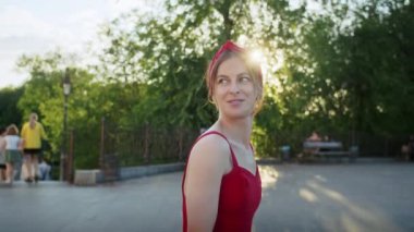 Kırmızı elbiseli mutlu kız parkta yürüyor, sokağın batan güneşinin tadını çıkarıyor, yaz yaşam tarzı.