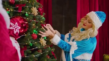 Noel Baba ve Bayan Noel Baba mutlu Noeller diliyor, hediyeler veriyor ve ağacı süslüyor.