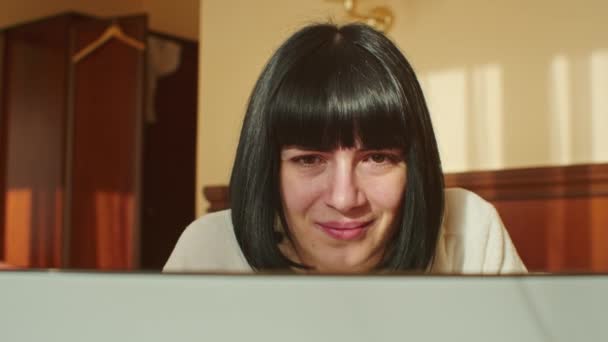 在这个视频中 一位年轻女性展示了如何在隔离期间平衡工作与舒适 她一边在家里的沙发上休息 一边高兴地在笔记本电脑上打字 — 图库视频影像