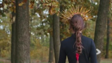 Santa Muerte makyajlı, siyah bir ölüm elbisesi giymiş genç bir kadın günbatımında ormanda sonbahar yapraklarının arka planına doğru yürüyor. Ölüler Günü veya Cadılar Bayramı konsepti