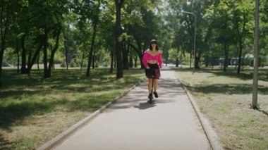 Neşeli kız yazın tadını çıkarıyor ve park ve şehir sokaklarında scooter sürüyor.