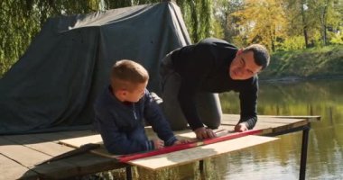 Mutlu baba ve oğul ağaçta bir ev inşa eder, bir çizime bakar, bir ağacı testereyle keser, tornavidayla kendi kendini becerir..