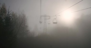 Sisli bir dağda kayak kaldırma sandalyeleri ve sislerin arasından bakan güneş..