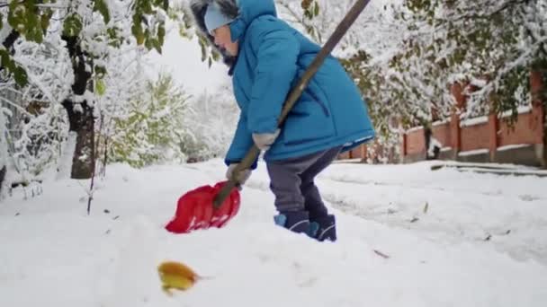寒い天候の中で小さな助手が 彼の街で嵐と戦って 道から氷をきれいにする — ストック動画