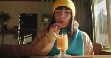 Güneşli bir kafede latte içen bir kadın. Rahatlama ve rahatlama konsepti. Yaşam tarzı blogu için tasarım, kahve dükkanı pazarlaması, menü tasarımı. Doğal ışıklandırmayla iç mekan.