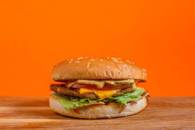 Ahşap bir yüzeyde marul, domates, peynir ve pastırma ile nefis bir çizburger. Turuncu arka planlı stüdyo çekimi. Fast food ve hoşgörü konsepti. Menü, poster ve afiş için tasarım.