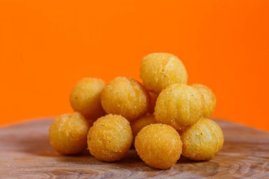 Tahtadaki altın peynir topları yığını. Turuncu arka planlı stüdyo çekimi. Atıştırmalık ve parti yemeği konsepti. Menü, poster ve afiş için tasarım.