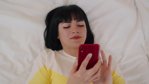 Γυναίκα Μαύρα Μαλλιά Ξαπλωμένη Στο Κρεβάτι Χρησιμοποιώντας Κόκκινο Smartphone Ψηφιακή — Αρχείο Βίντεο