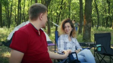 Ormandaki bir kamp alanında otururken arka planda çadırlarla sohbet eden bir çift. Açık hava iletişimi ve kamp yaşam tarzı konsepti. İlişki tavsiyesi yayını için tasarım