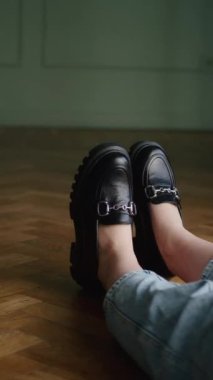Yuvarlak kotla siyah topaklı makosen giyen, ayakları ahşap zeminde oturan biri. Kopya alanı ile tasarım ve reklam için modaya uygun ayakkabı konsepti.