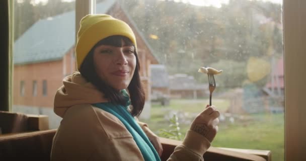 Жінка Шматочком Їжі Виделці Посміхаючись Біля Вікна Видом Тепла Внутрішня — стокове відео