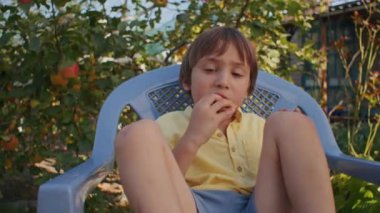 Sandalyede oturan bir çocuk bahçede bisküvi yiyor. Sıradan bir rahatlama ve basit zevkler konsepti. Yaşam tarzı blogu, aile eğlencesi makalesi için tasarım.