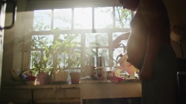 Yaşlı adam mutfağa su dökerken pencere kenarında bitkiler vardı. Arka plandaki pencerelerden gelen doğal ışık. Ev hayatı ve sabah rutini kavramı. Poster, afiş ve tebrik kartı için tasarım. Samimi