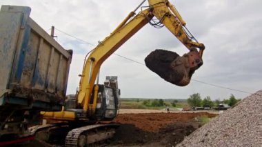 Kazıcı inşaat alanındaki bir çöp kamyonuna toprak yüklüyor. Açık havada çalışan ağır makineler..