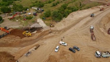 Ağır makineler, kamyonlar ve işçilerle dolu bir inşaat alanının havadan görüntüsü. Toprak taşıma ve kazı çalışmaları devam ediyor.
