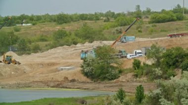 İnşaat iskeleti, ağır makineleri ve vinçleri olan suya yakın bir inşaat alanı. Toprak hareket halindeki açık hava manzarası.
