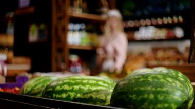 Markette sergilenen karpuzlar. Müşteriyle geçmişi bulanık ve ürünlerle dolu raflar. Alan fotoğrafçılığının sığ derinliği.