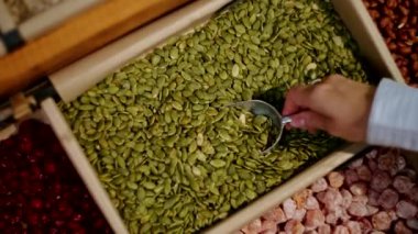 Toptan bir yiyecek dükkanındaki kağıt kutusundan balkabağı tohumları toplamak. Tohumları diğer kurumuş mallarla çevrili ahşap bir konteynıra yakın çekim yapın..