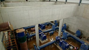 Büyük mavi boru hatları, motorları ve vanaları olan endüstriyel su pompalama istasyonu. İşçiler bir yeraltı tesisi içinde bakım ve kaynak yapıyorlar..