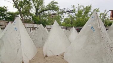 Endüstriyel bir inşaat sahasında depolanmış beton piramit şekilli bloklar. Güçlendirilmiş beton elementlerin üretimi ve depolanması.