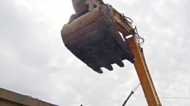 Kazıcı inşaat alanındaki bir kamyona toprak döküyor. Bulutlu gökyüzü altında yer değiştirme operasyonları sırasında ağır makineler çalışıyor. Sanayi ve inşaat fotoğrafçılığı.